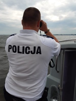 Zdjęcie pokazuje policjanta ogniwa wodnego obserwującego przez lornetkę regaty na wodzie