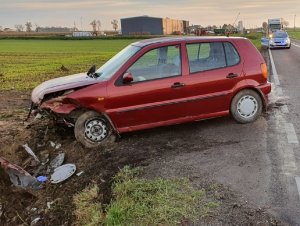 Zdjęcie z wypadku drogowego. z przodu na środku zdjęcia uszkodzony pojazd marki volkswagen koloru czerwonego