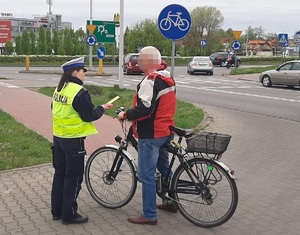 Policjantka rozmawia z rowerzystą i przekazuje opaskę odblaskową
